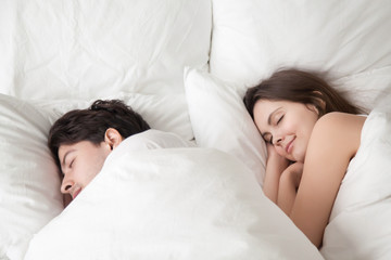 Young woman and man lying asleep in cozy big white bed at home under blanket, soft sleep, couple...