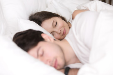 Happy couple resting together, enjoying soft bed and pleasant good dreams, beautiful girl smiling while sleeping with her boyfriend or husband between the sheets at home