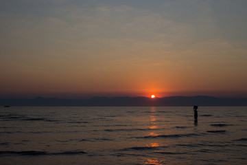 An African woman wades to fill her bucket for washing on Lake Malawi at sunrise.
