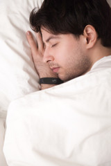 Close up vertical top view of man sleeping on white comfortable bed, wearing digital smartwatch or wristband tracker for monitoring and controlling his sleep. Keeping fit and healthy, time management