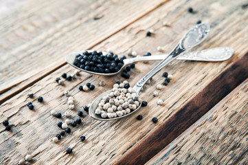 Mix of spices, peppercorns. Two metalic crossed teaspoons with black and white dried pepper grains...