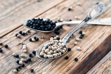 Mix of spices, peppercorns. Two metalic crossed teaspoons with black and white dried pepper grains on old vintage wooden table background. Closeup.
