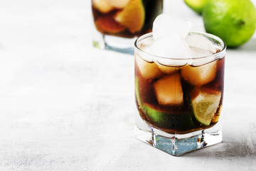 Alcohol cocktail with lime, ice and cola, gray background, selective focus