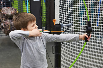 Little boy shoots by bow in children's shooting range