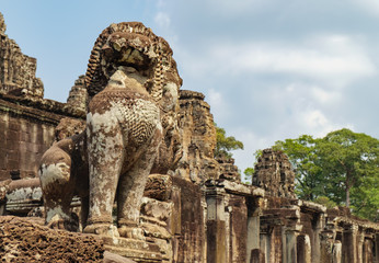 Fototapeta premium Lion in the foreground guards Prasat Bayon, central temple of Angkor Thom, Siem Reap, Cambodia. Ancient Khmer architecture and famous Cambodian landmark, World Heritage.