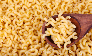 Pasta background. In the foreground there is a spoon in which are pasta. Pasta is spilled in the background. The background is out of focus.