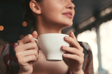 woman holding a cup of coffee in hand, sitting in the morning in a cafe and smiling - 144471051