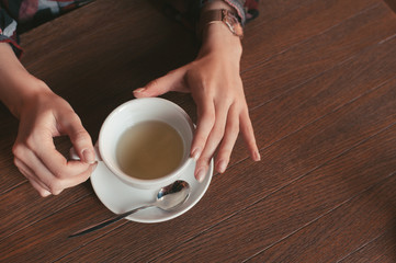 woman holding a cup of coffee in hand, sitting in the morning in a cafe