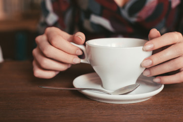 woman holding a cup of coffee in hand, sitting in the morning in a cafe
