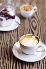 White cup of cappuccino coffee with yogurt and granola  on a wooden textured table