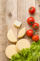 Top view on cut cheese heads on wooden board served with tomatoes and fresh salad. Serving French homemade cheese. Food concept