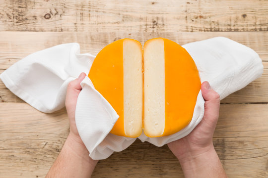 Top view on cut cheese head in yellow vacuum pakage in man's hands on wooden board. Serving French homemade cheese. Food concept