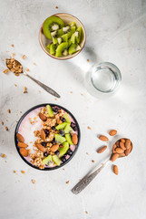 Healthy diet breakfast: smoothies bowl, with yogurt, fresh blueberries (black currant), kiwi, granola oatmeal, almond nuts. On a white stone table, with water and ingredients. Top view copy space