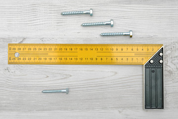 A yellow angle ruler and four metal bolts horizontally placed on white wood background.