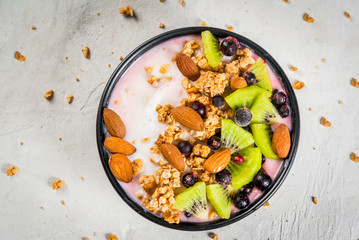 Healthy diet breakfast: smoothies bowl, with yogurt, fresh blueberries (black currant), kiwi, granola oatmeal, almond nuts. On a white stone table, with water and ingredients. Top view copy space