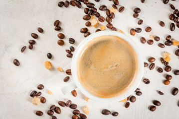 Morning. Food background. Grains of coffee, a cup of freshly brewed coffee and a spoon of brown cane sugar on a white stone table. Top view