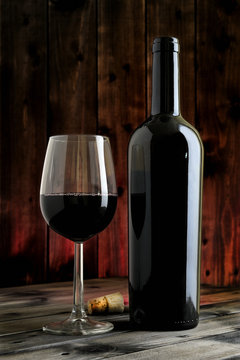 Closeup of red wine glass and bottle, on an antique wooden table.