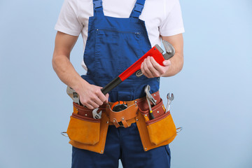 Handsome young plumber with tools on color background