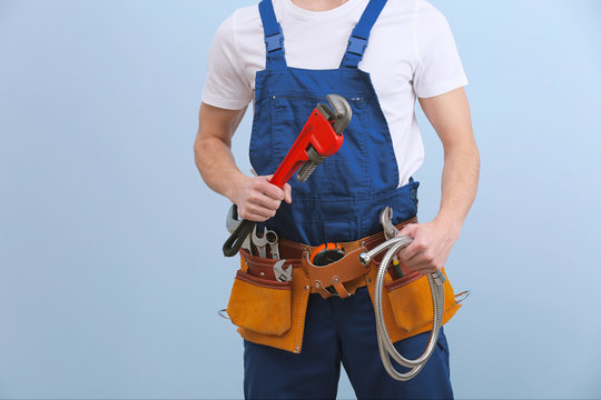 Handsome young plumber with tools on color background