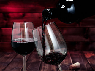 Red wine poured from a bottle in a elegant crystal goblet, on an antique wooden table.