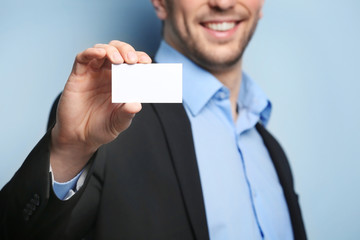 Young man with business card on color background, closeup