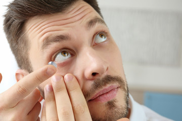 Young man putting contact lenses at home, closeup