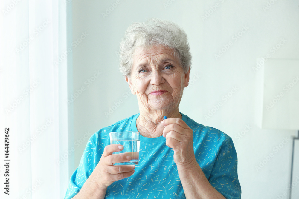 Poster elderly woman taking pill at home