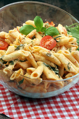 Penne pasta in tomato sauce with chicken, tomatoes decorated with basil on a wooden table