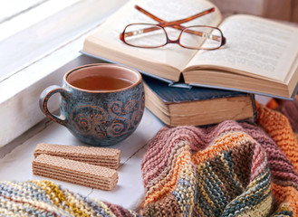 Cozy morning at home. A cup of tea, a blanket, old books and glasses on the windowsill, selective focus. 