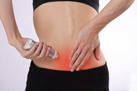 Woman suffering from back pain applying pain relief cream . Sports exercising injury.