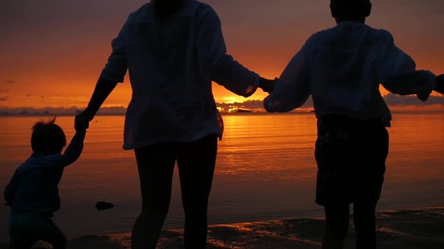 family holding hands running on the beach towards the sea at sunset time