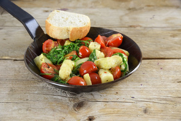 fried vegetables in a black pan with asparagus, tomatoes and spinach on a rustic wooden table
