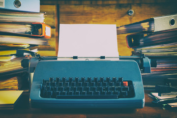 Chaos in retro office, old vintage typewriter and high stacks of folders on the desk 
