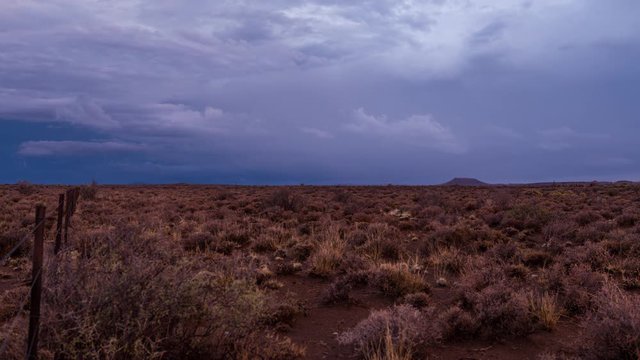 A static timelapse of a typical Karoo farm landscape in soft magenta and blue light with various cloud movements and a dramatic sky getting darker as the night falls