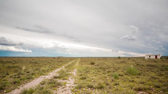 Static timelapse of a typical Karoo farm landscape with a small house next to a fence post with scattered clouds in a vast open scene available on request.
