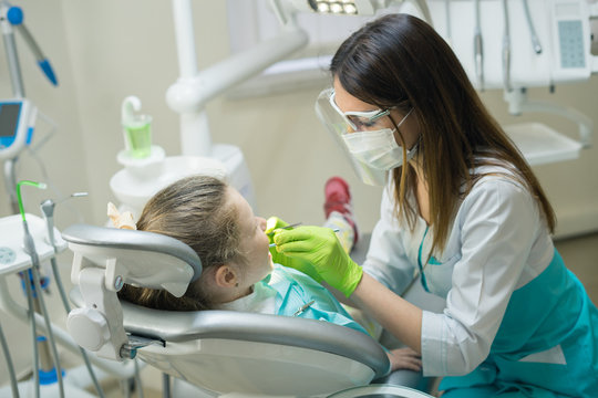 Female Dentist checking little cute girl patient at dental clinic. She is inspecting her mouth.