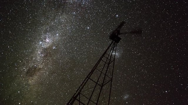 Linear & pan night timelapse of a silhouette Windmill frantically blowing in the wind against the Milky Way in a dark night sky with a reverse focus pull from out of focus to in focus