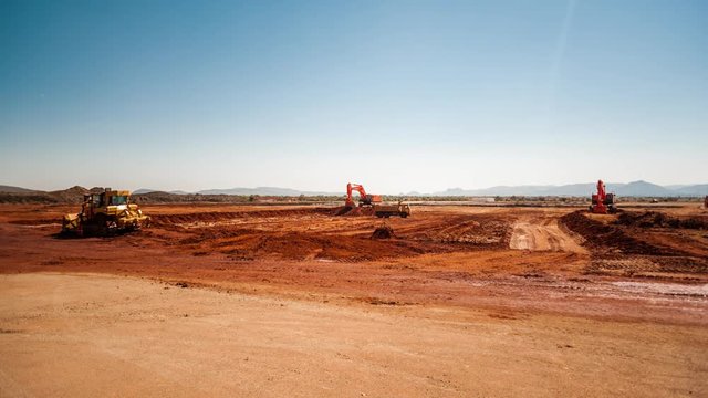 Static pan timelapse of a construction site on a mine while earthworks is in progress with heavy load machinery, trucks and tippers close to action