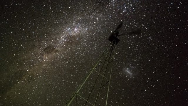 Linear & pan night timelapse of a silhouette Windmill frantically blowing in the wind against the Milky Way in a dark night sky with a reverse focus pull from out of focus to in focus