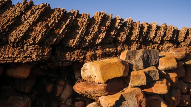 A linear and pan timelapse of a textured wall of a historical barn made with stacks of rocks and cow dung with shadows moving across the frame available on request.