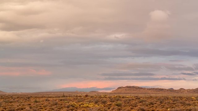 A beautiful static timelapse of a typical Karoo farm landscape in soft warm magenta light with various cloud movements, typical of an old artist painting