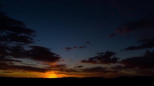 A static timelapse at sunset with a dramatic cloudy sky and contrasty blue and orange glow as the shot dip to black