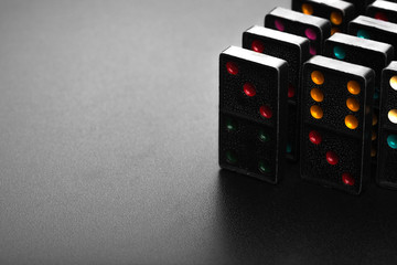 Black color dominoes with colorful dot game pieces lying on dark background