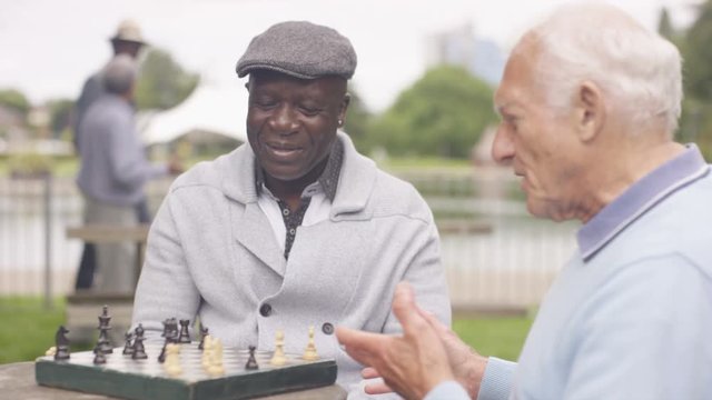  Happy senior male friends relaxing in the park playing chess