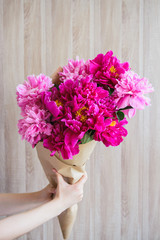 white caucasian girl holding red and pink peonies bouquet at wood wall backdrop