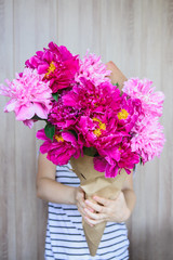 happy white caucasian girl holding red and pink peonies bouquet in front of face at wood wall backdrop