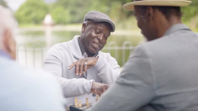  Portrait smiling senior man playing chess in the park with a friend