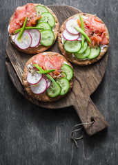 Crispy whole wheat cracker with smoked trout, cucumber and radish. Healthy snack. On dark wooden background, top view