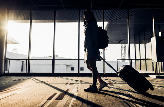 Silhouette of young girl walking with luggage walking at airport terminal window at sunrise time,travel concept,journey lifestyle