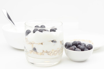 Glass Cup with yogurt, oatmeal and blueberries, next to the dishes with ingredients.